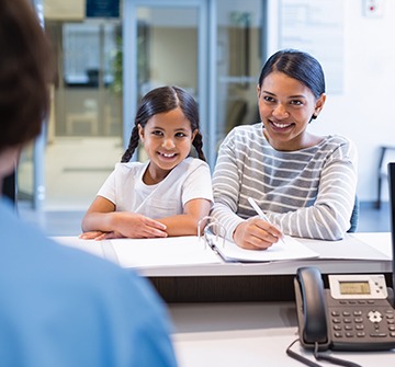 Mother and daughter completing payment forms at dental office reception desk