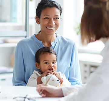 Mother holding child in lap talking to dental team member