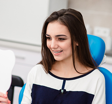 Young woman with traditional braces smiling at reflection