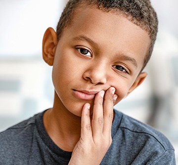 Young child in need of emergency kids dentistry holding cheek in pain