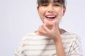 Woman smiling while putting on Invisalign aligner