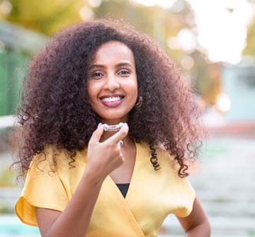 Woman smiling outside while holding Invisalign clear aligner