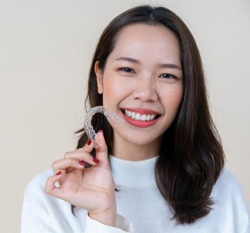 Woman in white shirt smiling while holding Invisalign