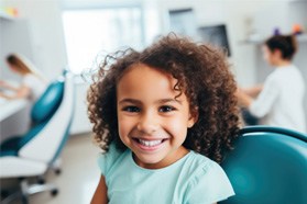 Child with curly hair smiling in dental chair