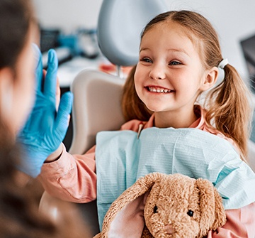 Child with pigtails smiling while giving pediatric dentist high-five