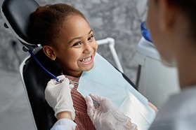 Pediatric dentist placing bib over smiling child in treatment chair