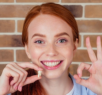 Young woman holding up tooth after extraction