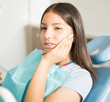 Teen in need of emergency dentistry holding cheek in pain