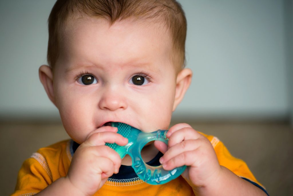 Infant in yellow shirt chewing on blue toy